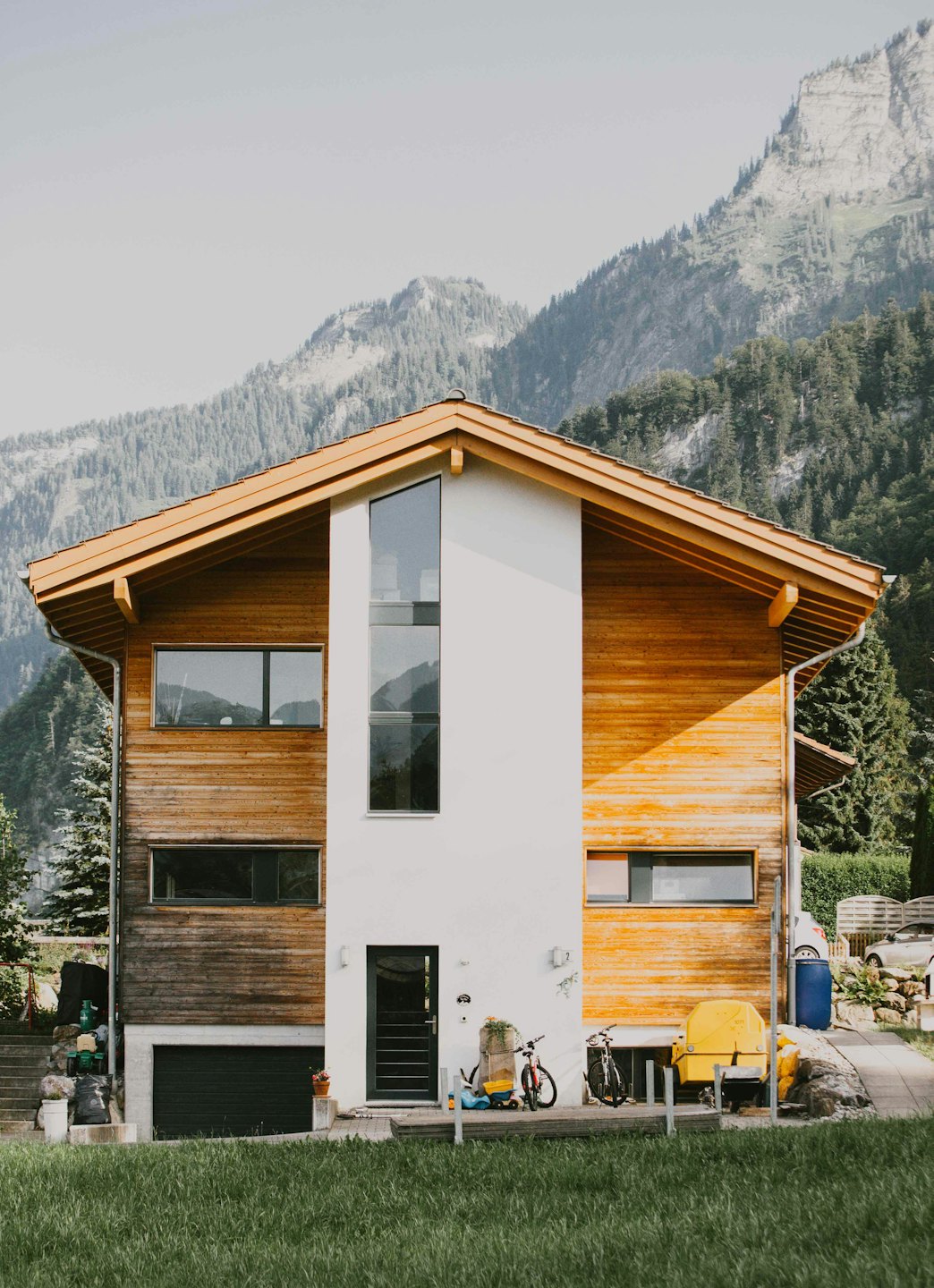 Modern house with bicycles and equipment sits before pine mountains.